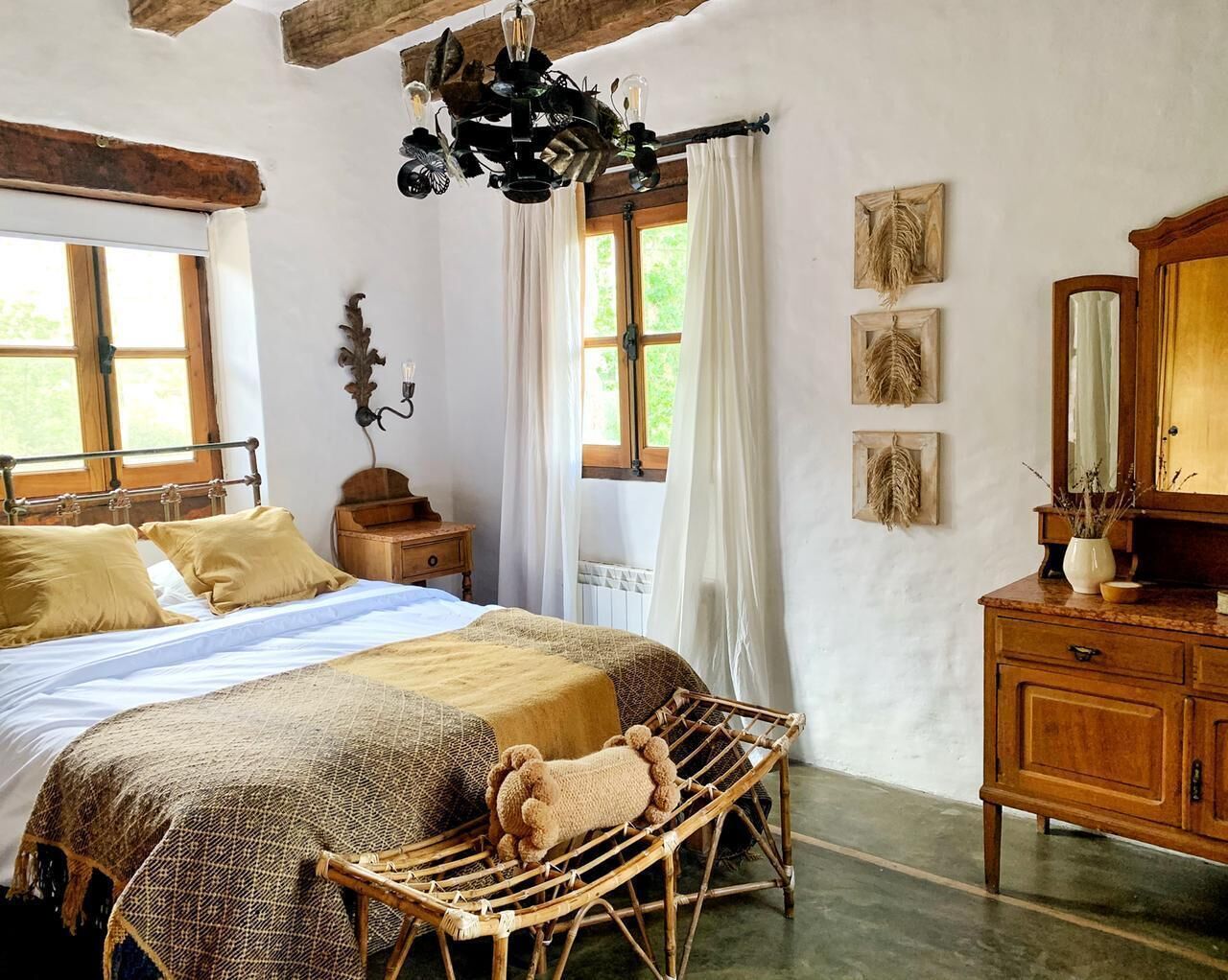 Un dormitorio rústico con una cama grande, cabecera de madera, un aparador de madera y una silla de mimbre.