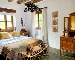 Um quarto rústico com uma cama grande, cabeceira de madeira, cômoda de madeira e uma cadeira de vime.