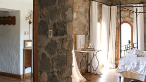 A stone-walled bedroom with a four-poster bed, a wooden floor, and a mirror on the left wall.
