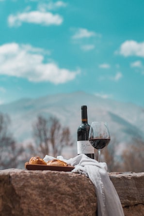 A bottle of wine and a glass on a stone ledge with pastries, set against a mountain backdrop. - Castillo de Piedra Hotel Boutique (Tafi del Valle)