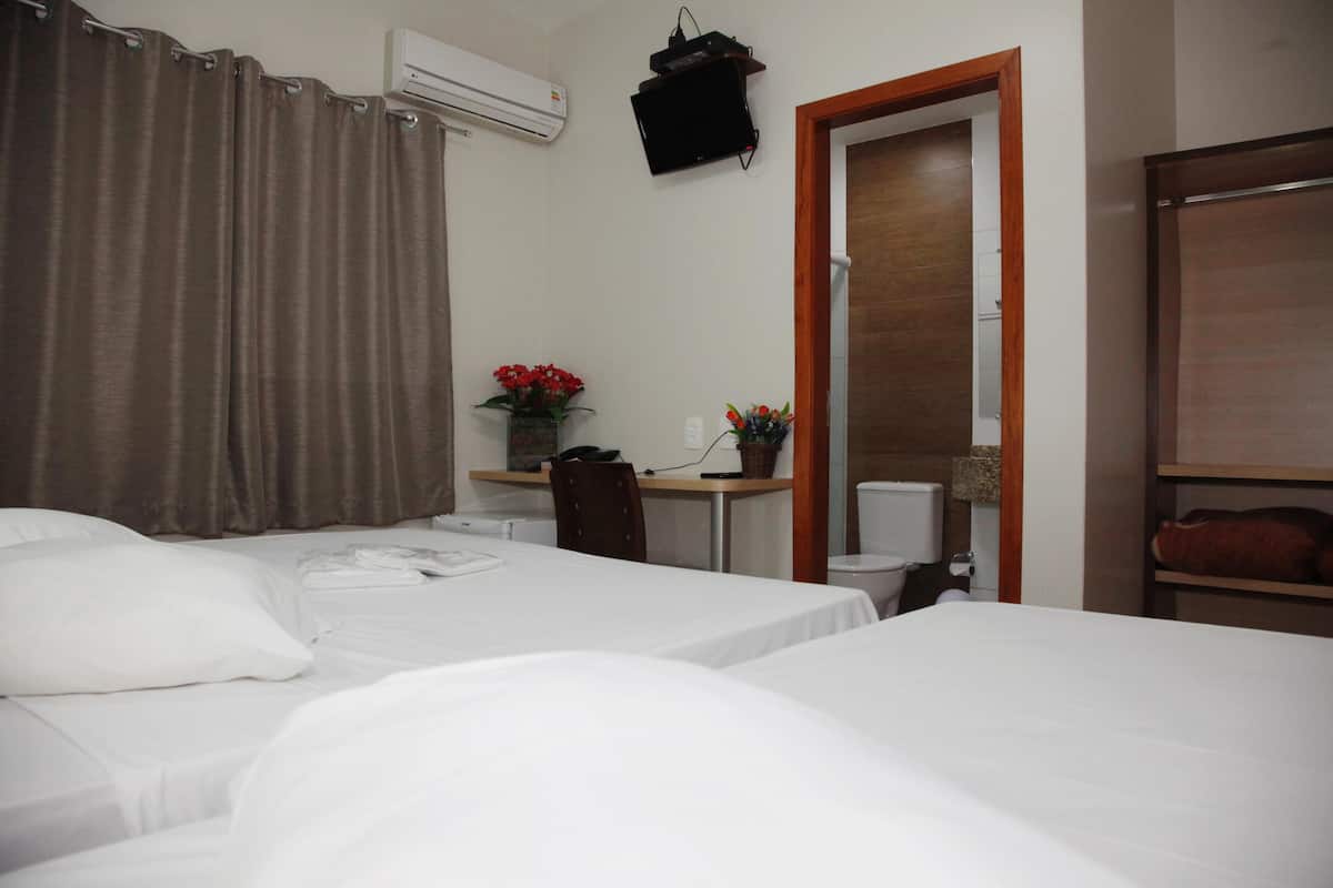 A hotel room with two beds, a desk with a chair, a small table with flowers, a television, and a wooden wardrobe.
