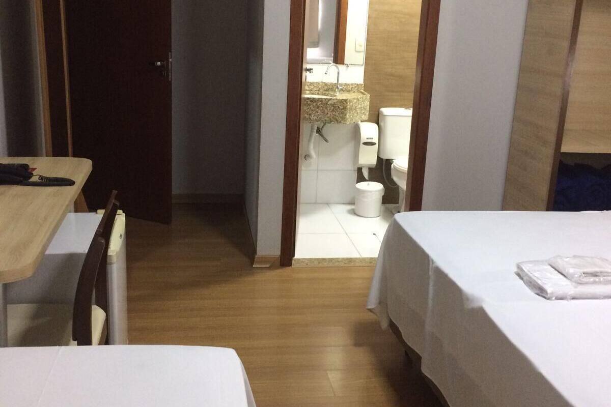 A hotel room with two beds, a wooden floor, a bathroom visible through an open door, and a small table with a chair.