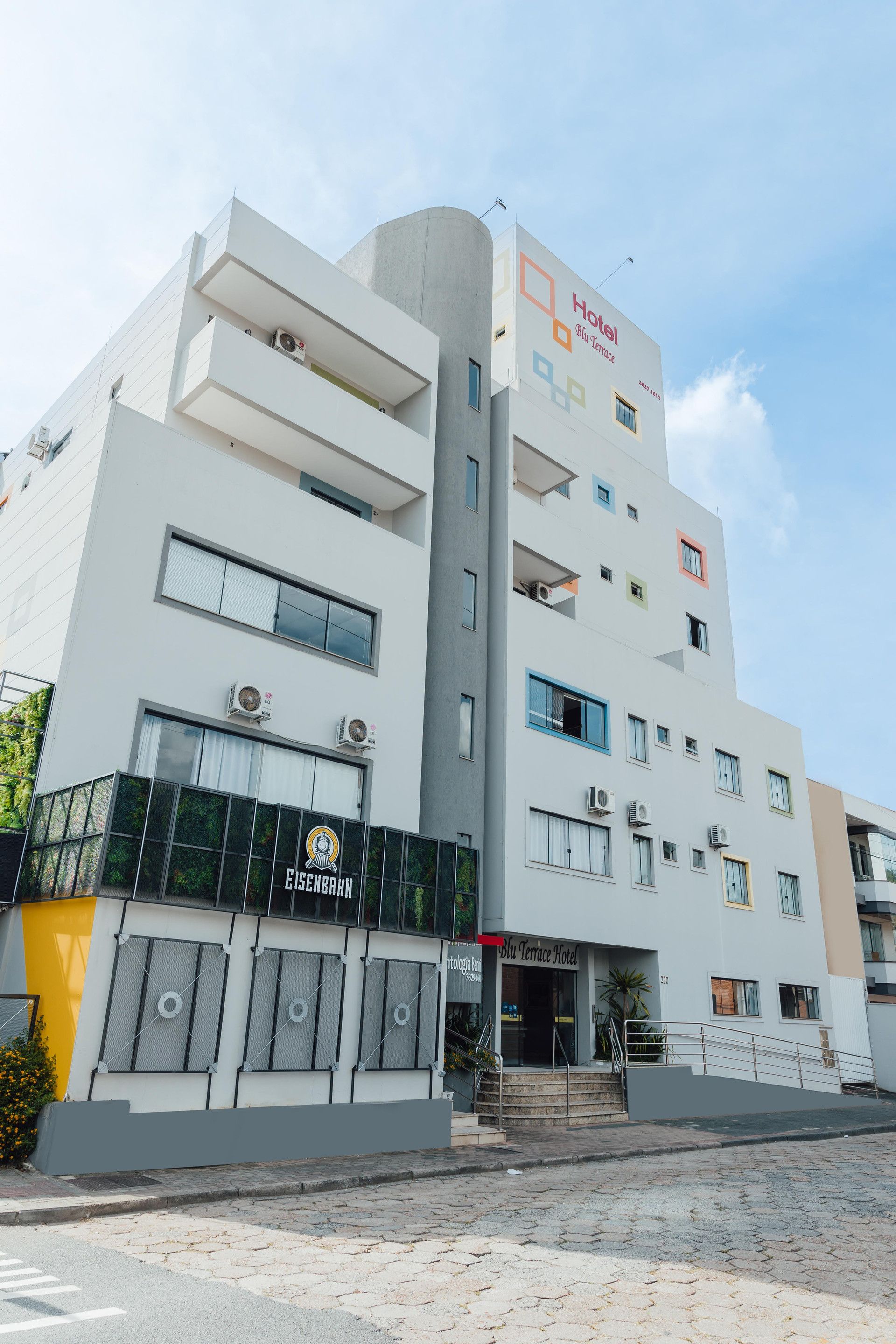 Um hotel com vários andares, varandas, aparelhos de ar condicionado e uma placa com o nome Blu Terrace Hotel.