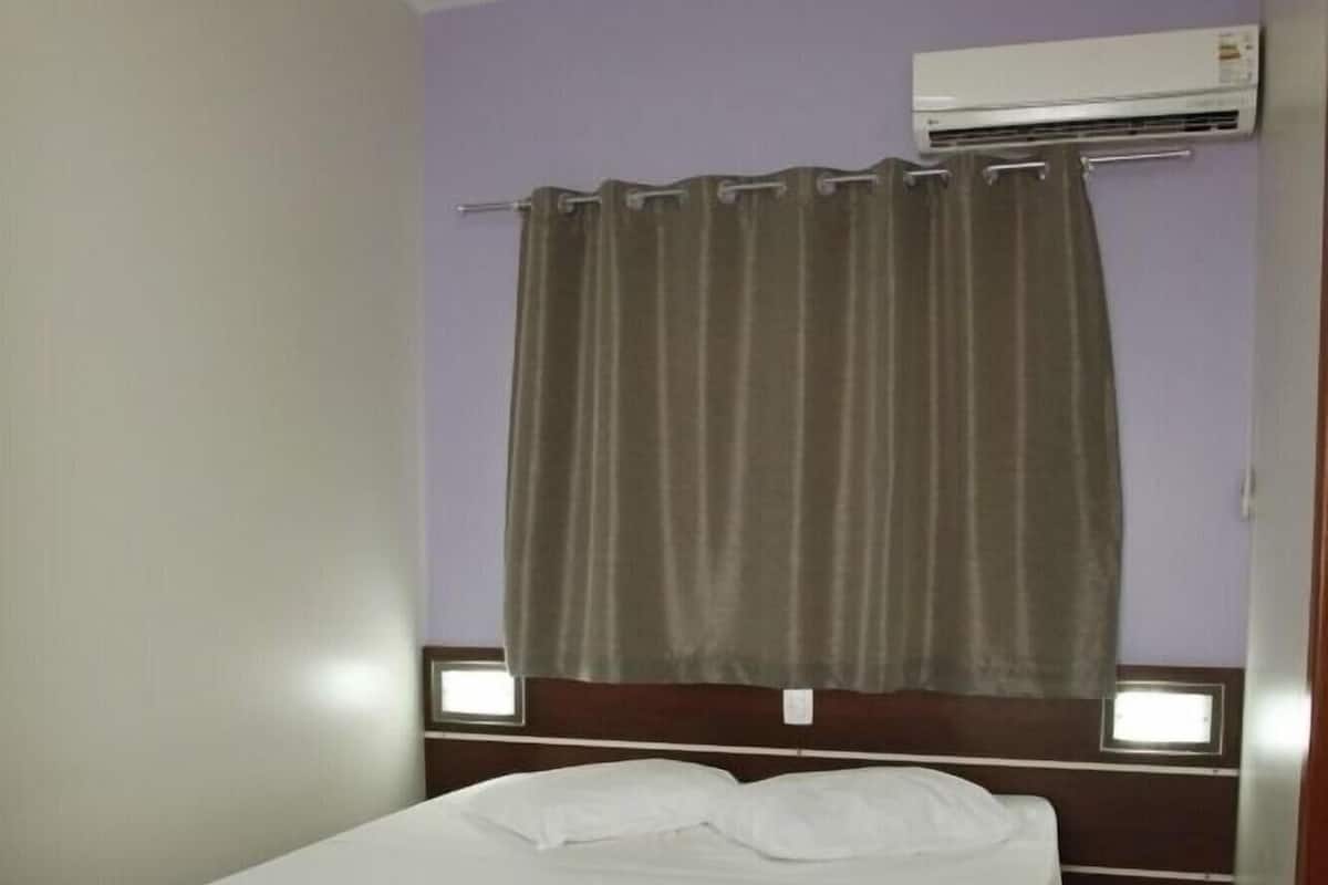 A single bed with a white bedspread in a room with purple walls and a wooden floor.