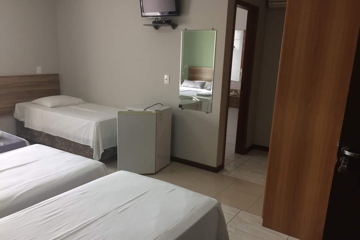 A hotel room with two beds, a small refrigerator, a television mounted on the wall, and a mirror.