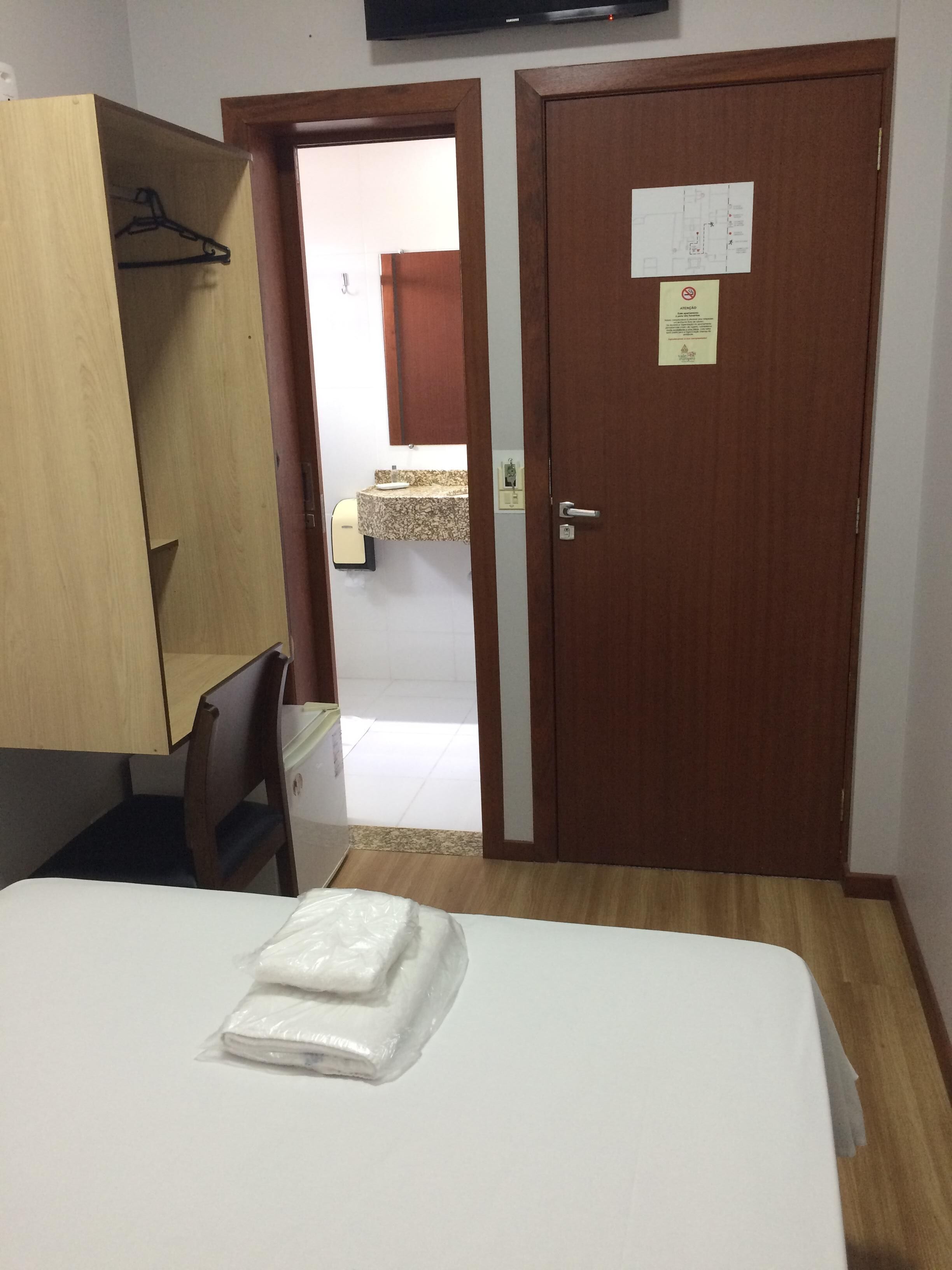 A hotel room with a bed, a wooden wardrobe, a desk, and a television.