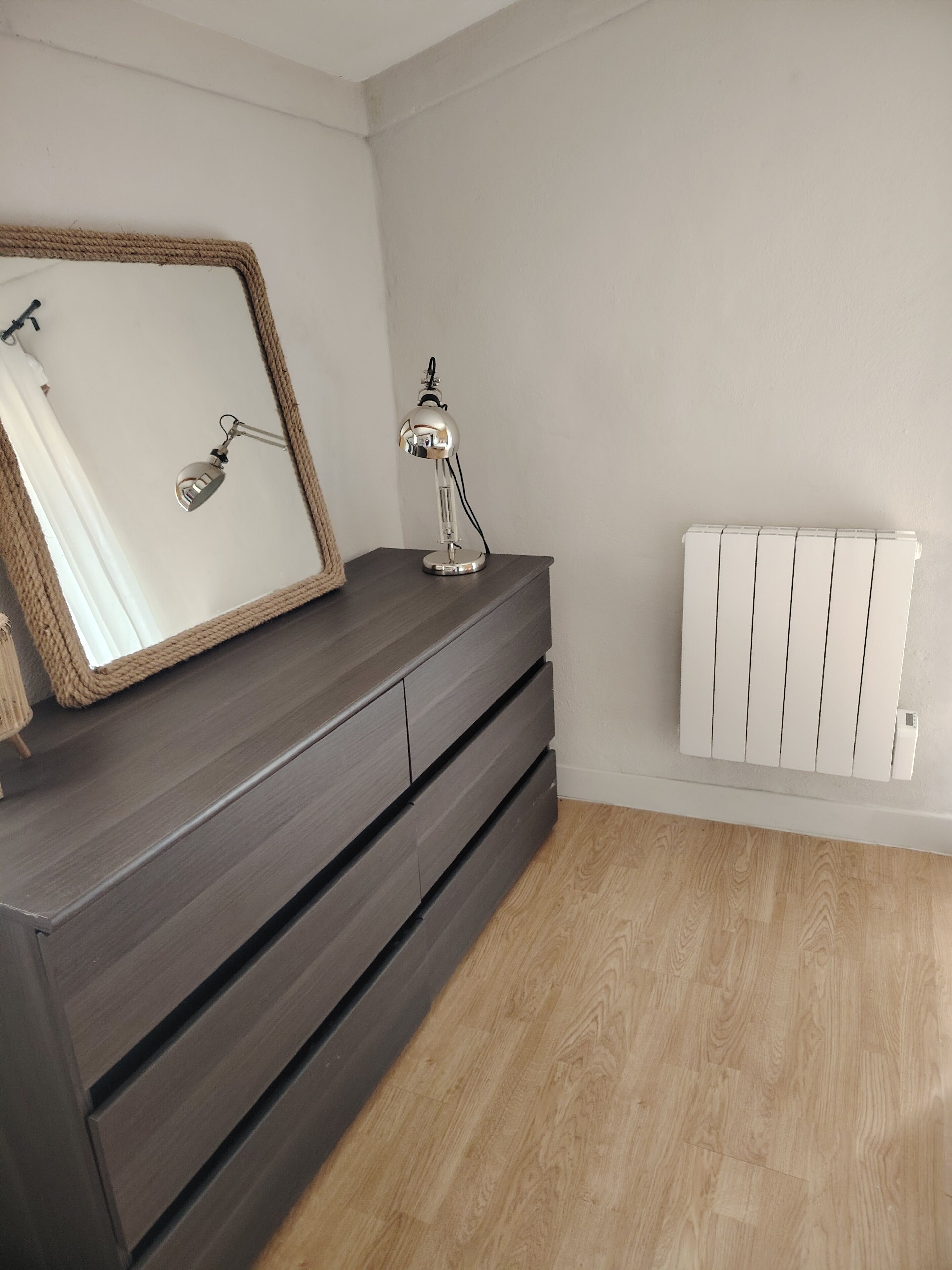 A room with a dark wooden dresser, a mirror, and a desk lamp.