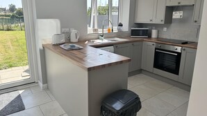 A modern kitchen with grey cabinets, a wooden countertop, a built-in oven, and a window overlooking a garden. - Newly Renovated 3 bed House Near Beach in Heacham (King's Lynn)