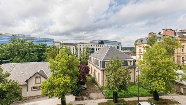 Un quartier résidentiel où se côtoient des bâtiments à l’architecture moderne et traditionnelle, notamment un grand immeuble à la façade vitrée et plusieurs maisons dotées de toits à pignon et de cheminées.