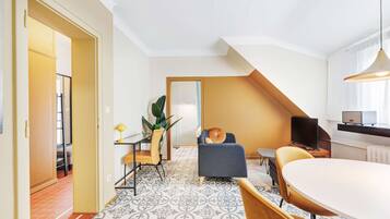 Una habitación de hotel moderna con comedor, sofá, televisión y escalera.