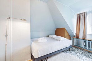 A bedroom with a sloped ceiling, a bed with white linens, a bedside table, and a radiator. - Stylish Apartment w/ Full Kitchen & Workspace (Luxembourg)