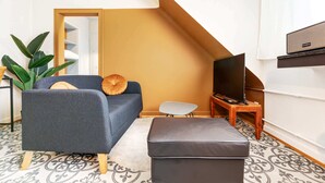 Un salon moderne avec un canapé gris, une petite table, un téléviseur et un escalier menant à l’étage supérieur.
