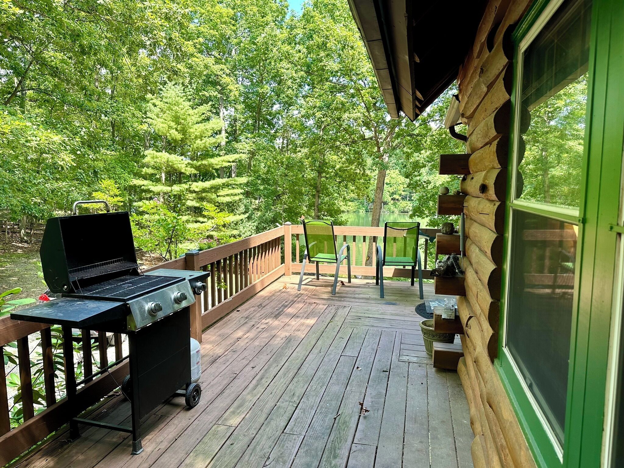 A wooden deck with a grill and outdoor furniture, surrounded by trees.
