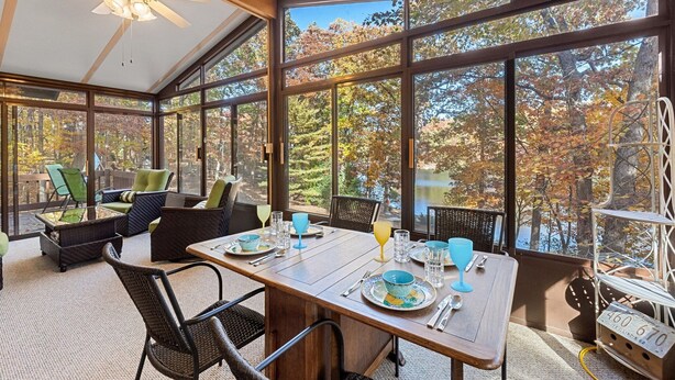 A sunroom with a large glass wall, a dining table set for four, and a ceiling fan. - Log Cabin w/ Hot Tub & Waterfront Patio! (Harpers Ferry)