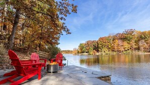 A lakeside deck with red Adirondack chairs and a fire pit. - Log Cabin w/ Hot Tub & Waterfront Patio! (Harpers Ferry)