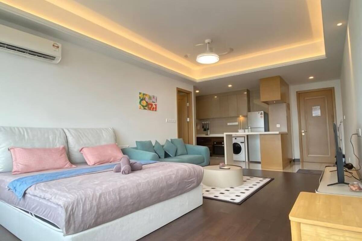 A modern living room with a sofa, a bed, a coffee table, and a kitchen area in the background.