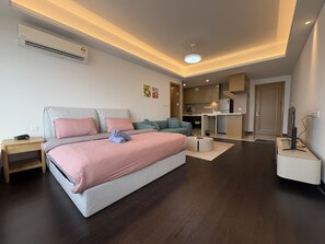 Une chambre moderne avec un grand lit, un canapé, un petit coin cuisine et une télévision.