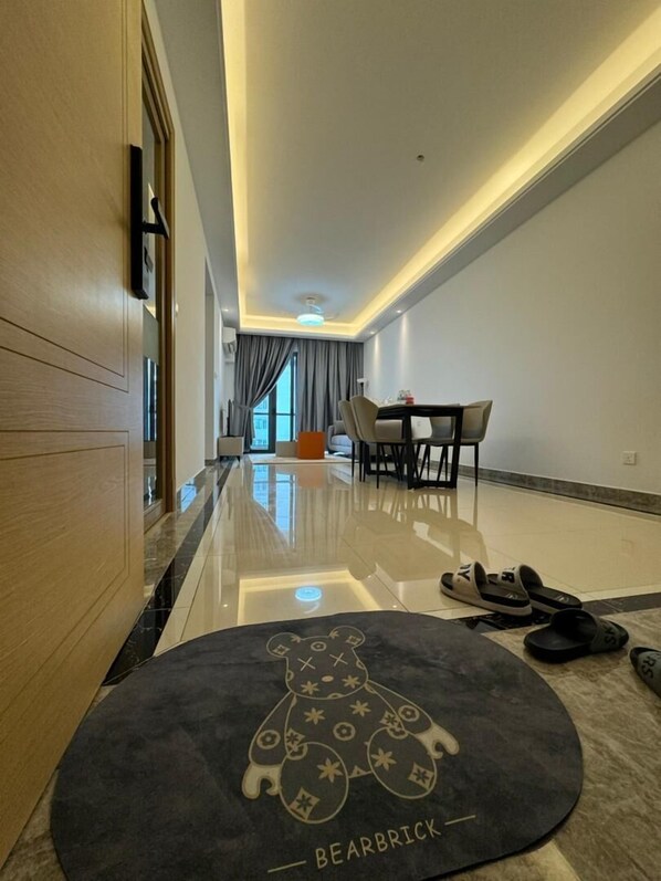 A modern hotel room with a wooden door, a dining area with a table and chairs, and a bear-themed rug on the floor. - R&F Seine Region (Johor Bahru)