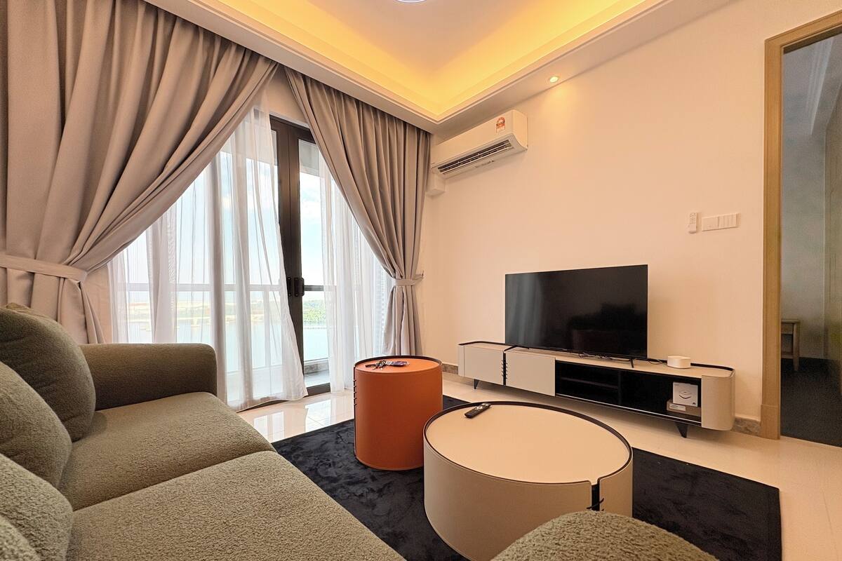 A modern living room with a sofa, ottoman, and a flat-screen TV.