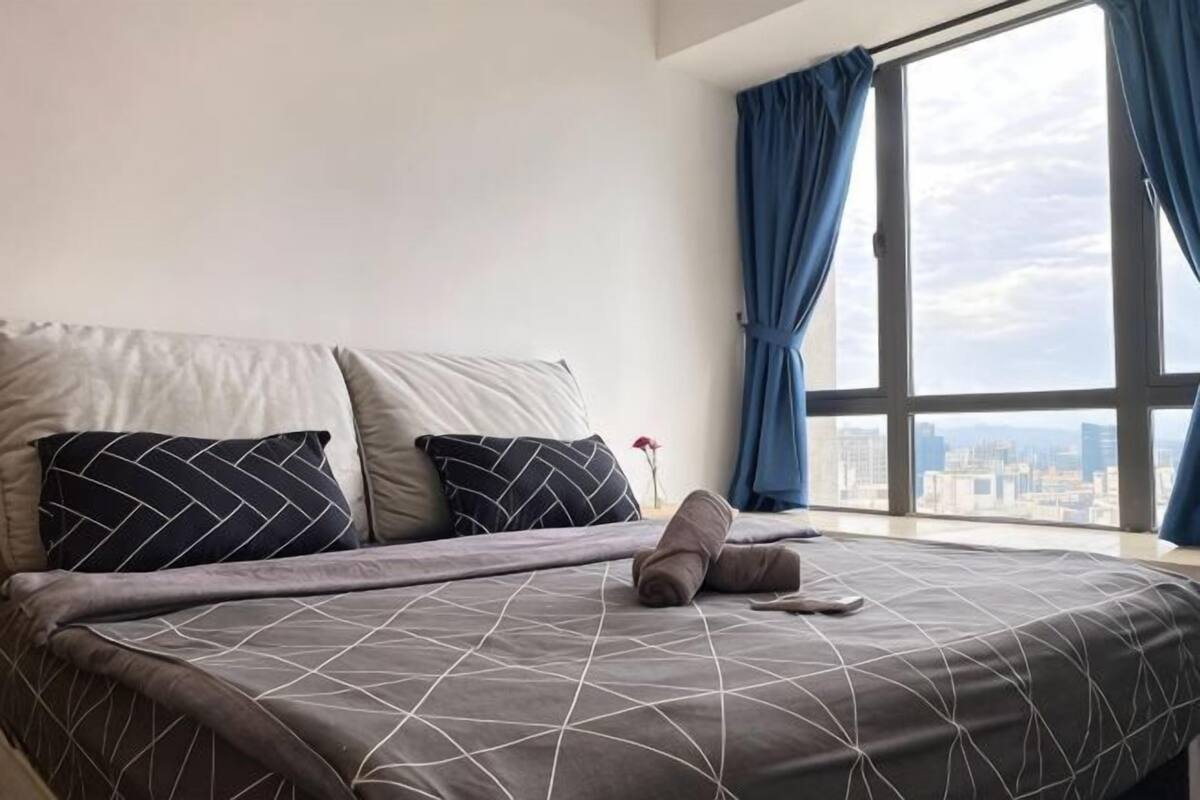 A bed with a geometric-patterned bedspread, two pillows, and a pair of slippers on the bed.