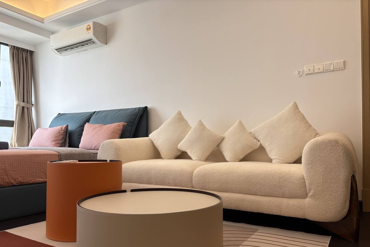 A modern living room with a beige sofa, a round table, and a large air conditioning unit on the wall.
