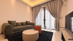 A modern living room with a sofa, a round ottoman, and a flat-screen TV. - R&F Seine Region (Johor Bahru)