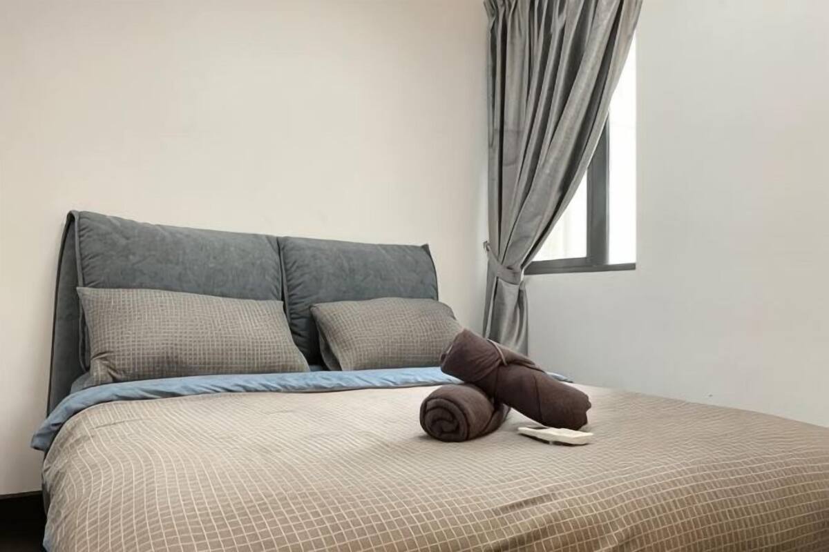 A bed with a headboard, pillows, a blanket, and a rolled towel.