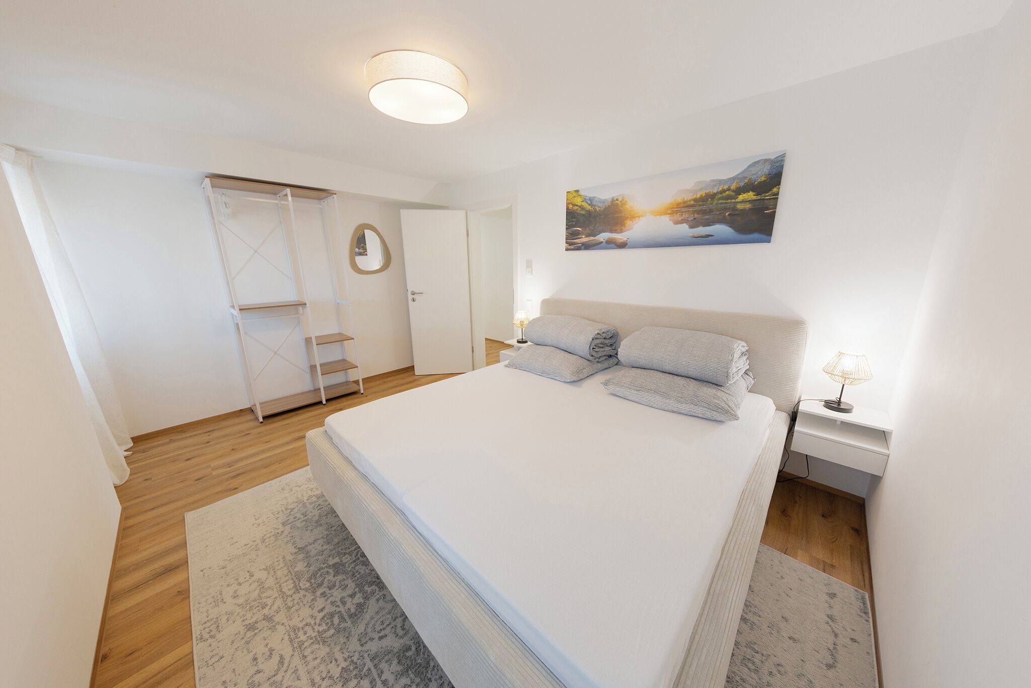 A bedroom with a bed, a nightstand, a lamp, a painting, and a wardrobe.