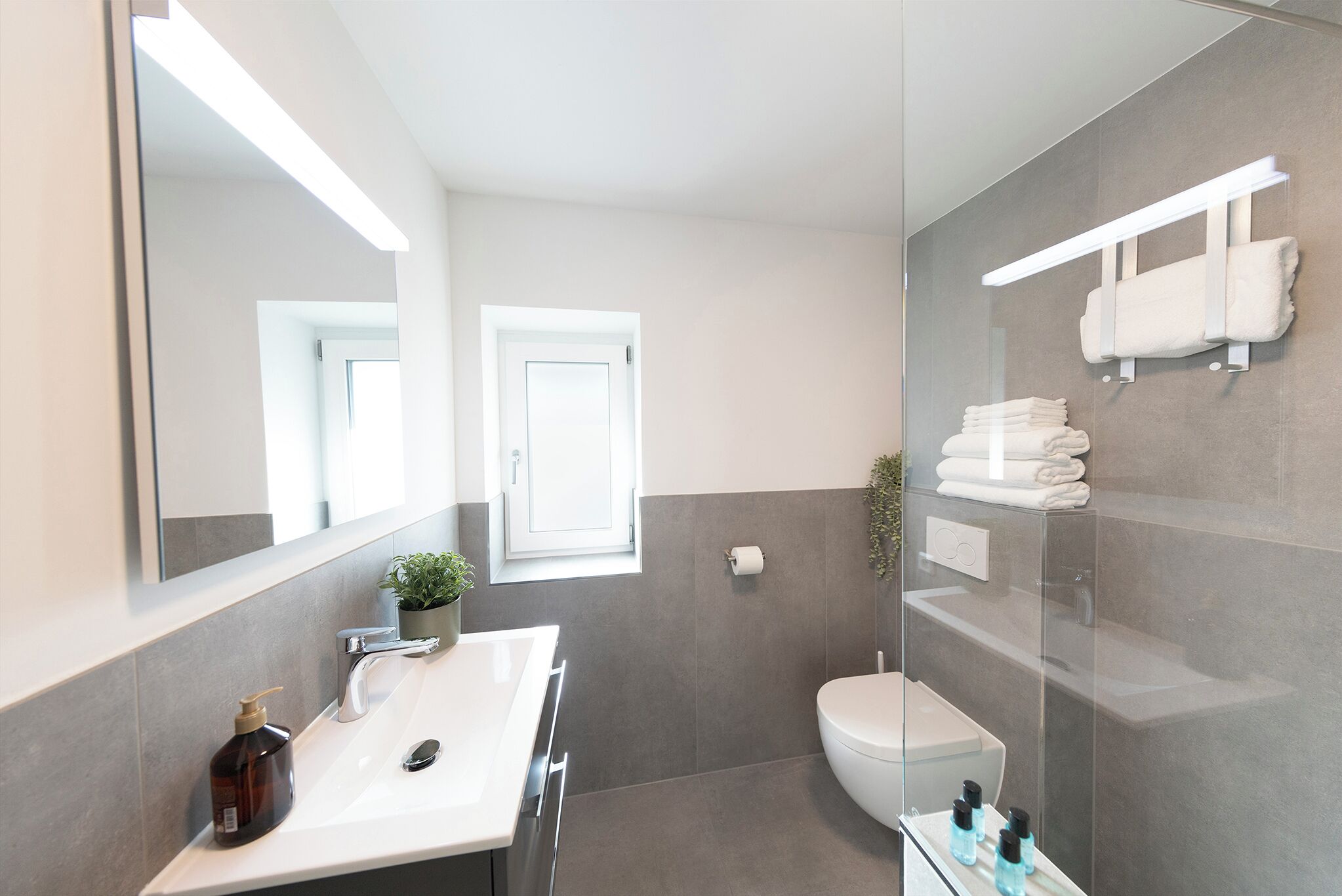 Une salle de bain moderne avec un grand miroir, un lavabo, des toilettes et une douche à parois de verre.