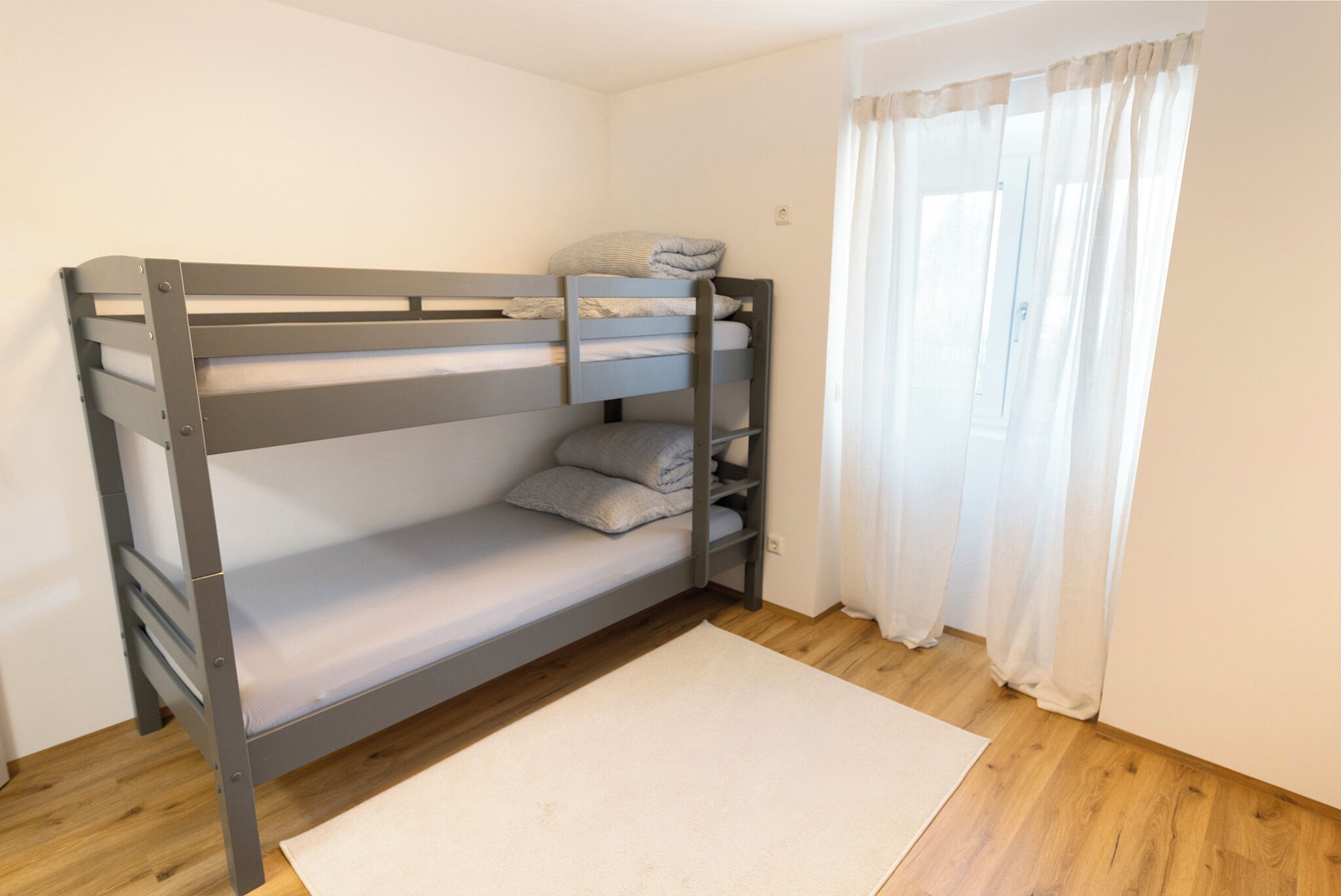 Una cama en literas en una habitación con suelo de madera y alfombra blanca.