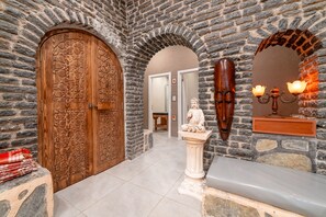 Un pasillo de paredes de piedra con una puerta de madera, una estatua y un banco.