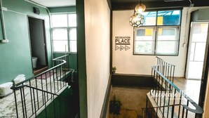 A hostel interior with a staircase, a wall sign reading "RECREATION PLACE", and a window with a view. - Sleepcase Hostel (Bangkok)