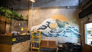 A room with a mural of a wave, a wooden reception desk, and shelves with books and shoes. - Sleepcase Hostel (Bangkok)
