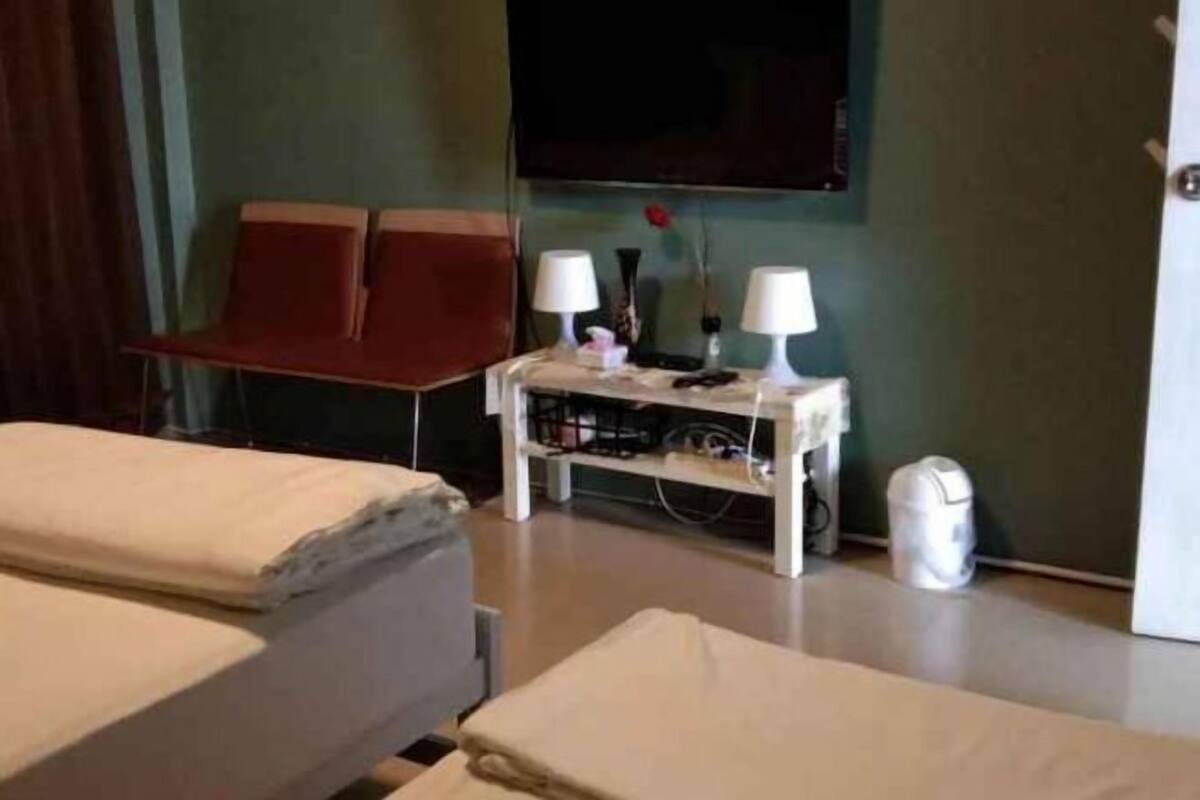 A hotel room with two beds, a small table with lamps, a TV, and a trash bin.