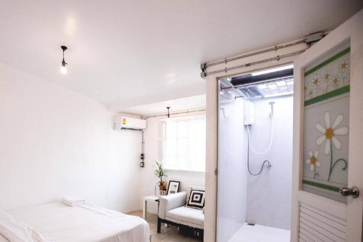 A bedroom with a bed, a chair, a small table with a plant, and a shower area with a glass door.