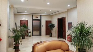 Et hotel lobby med elevator i midten, krukker med planter og en lædersofa.