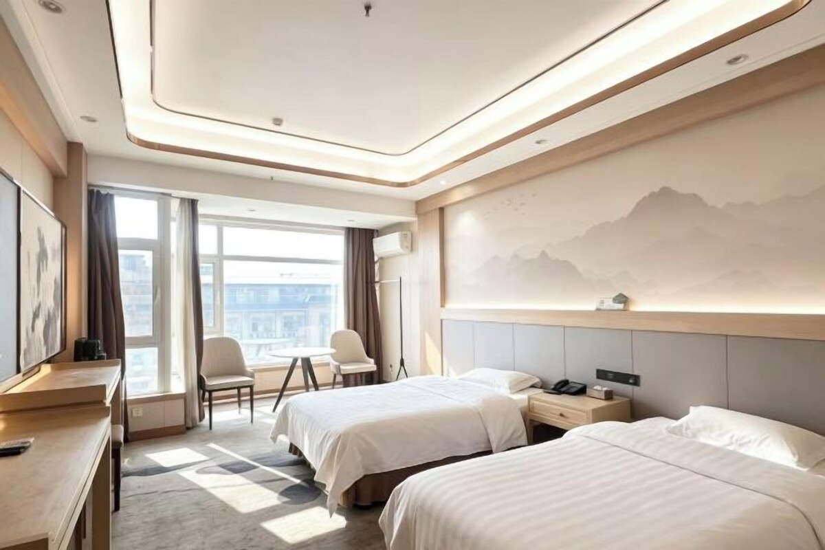 A hotel room with two beds, a desk, a chair, and a large window.