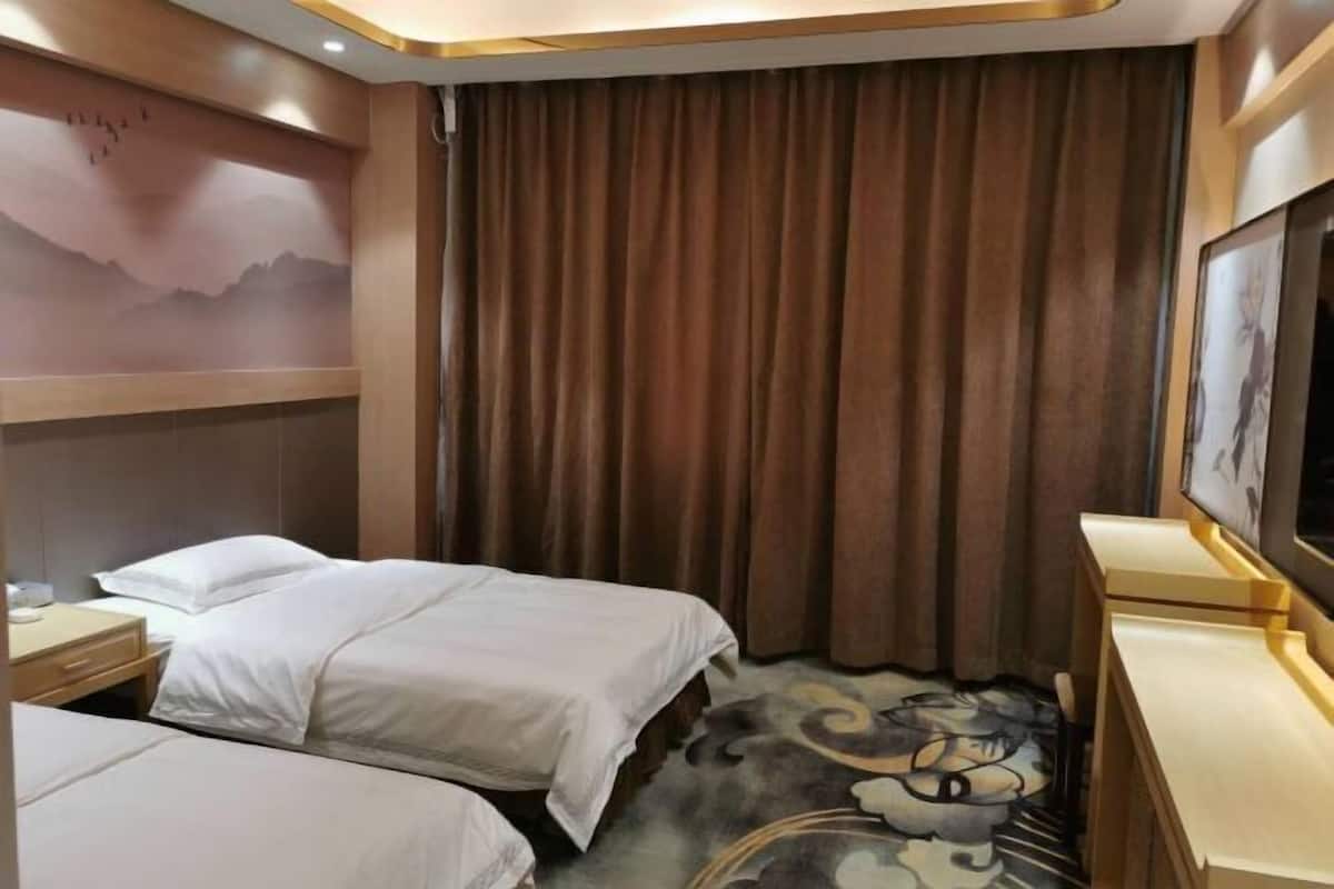 Habitación de hotel con dos camas, un ventanal con cortinas, un televisor de pantalla plana y un cuadro de paisaje montañoso en la pared.