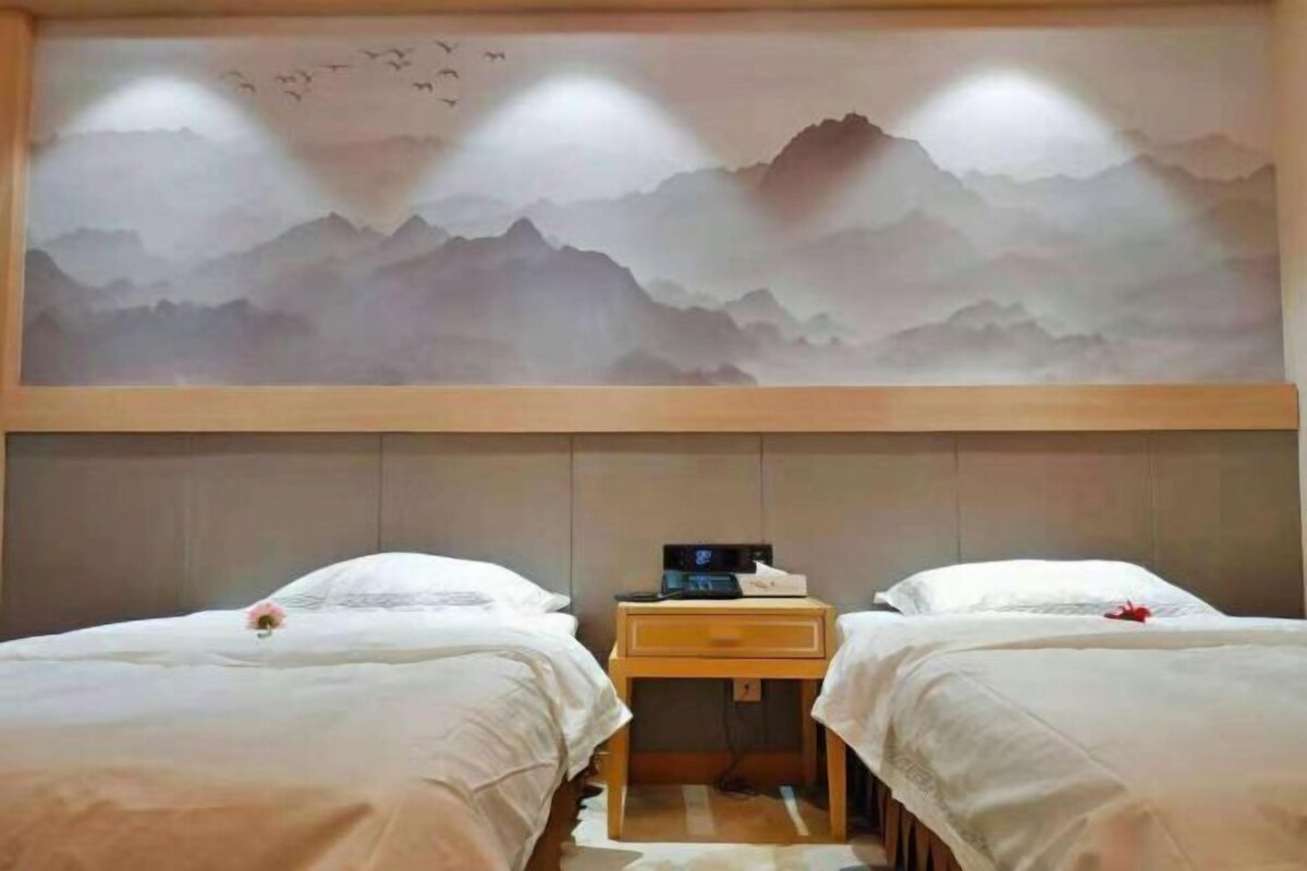 A hotel room with two beds, a wooden nightstand, and a wall mural of mountains.