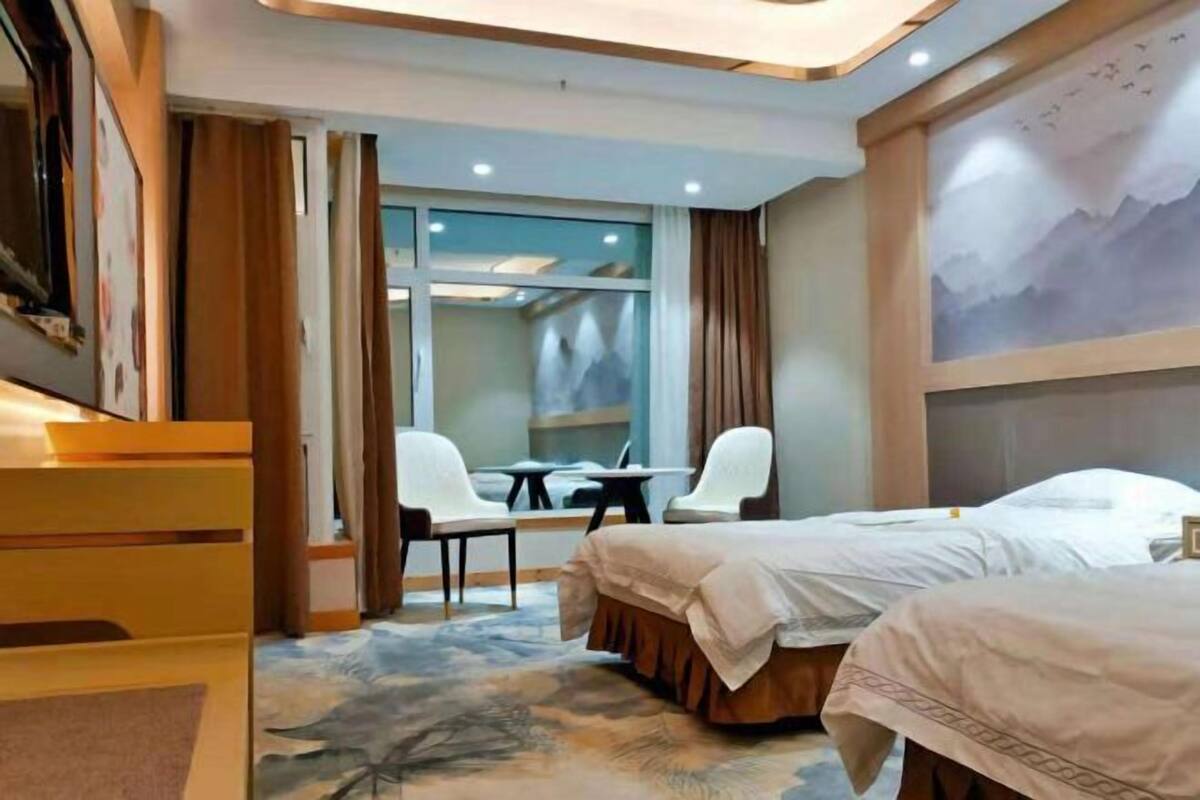 Una habitación de hotel con dos camas, un escritorio, sillas, un ventanal grande y un cuadro en la pared.