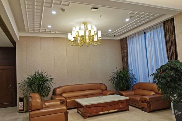 A living room with a brown leather sofa set, a wooden coffee table, and a chandelier. There are two potted plants and a large window with curtains. - Jinhai Hyatt Hotel Linyi (Linzhang)