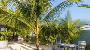 A patio area with a white table and chairs, surrounded by palm trees and plants. - La Solara Villa (Ukulhas)