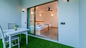 A modern room with a sliding glass door leading to a bedroom. The room features a white table with a chair, a small plant, and a ceiling fan. - La Solara Villa (Ukulhas)