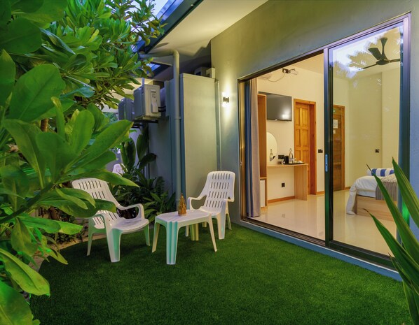 A modern hotel room with a sliding glass door leading to a balcony, a small table with chairs, and a bed with a striped pillow. - La Solara Villa (Ukulhas)