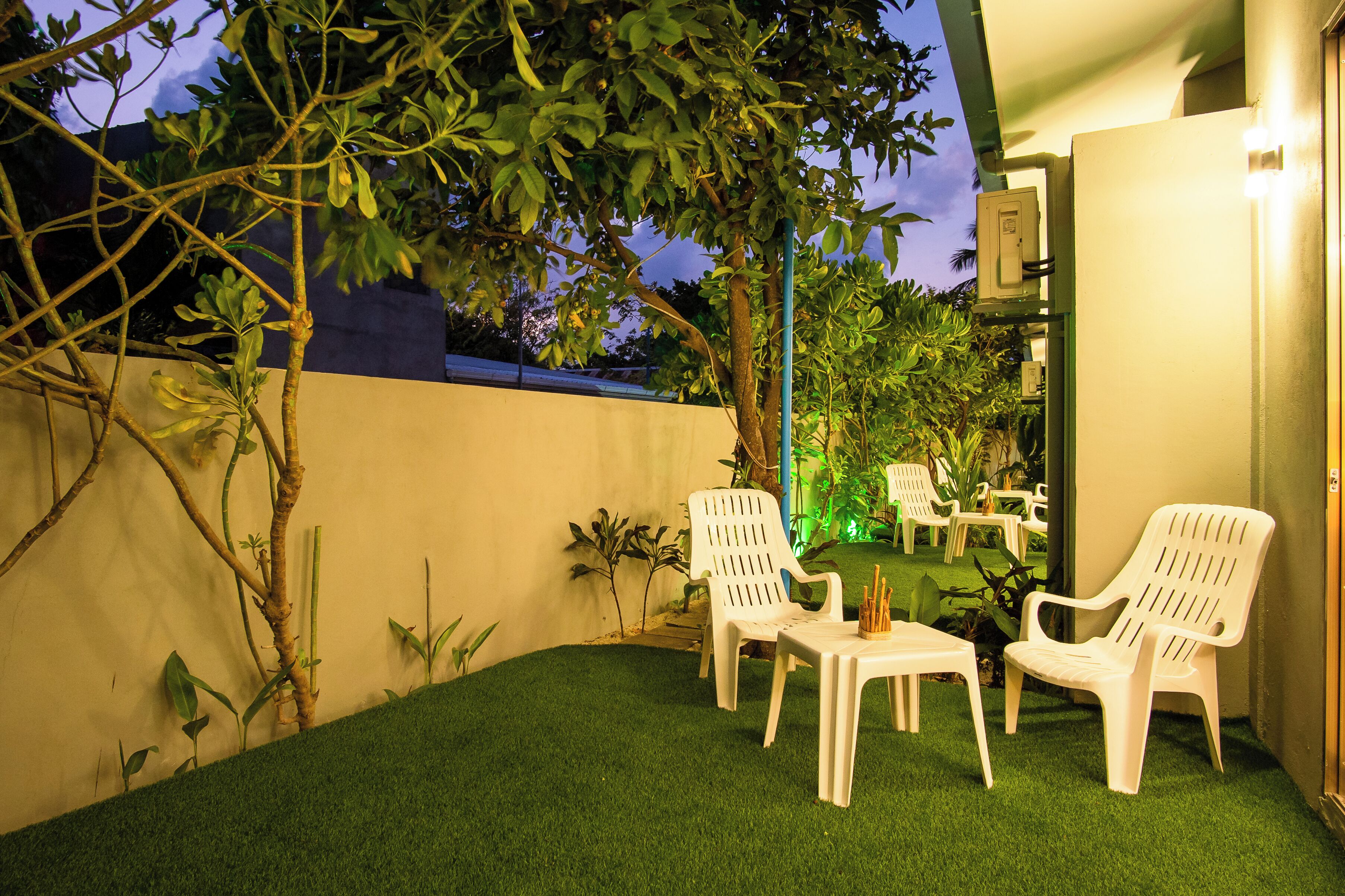 An outdoor patio with artificial grass, white plastic chairs, and a small table.