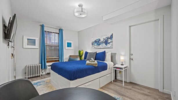 Un dormitorio moderno con cama, mesita de noche y ventana con cortinas.