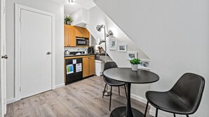 Una cocina compacta con microondas, estufa y armarios de madera. Cuenta con un comedor con una mesa y dos sillas.
