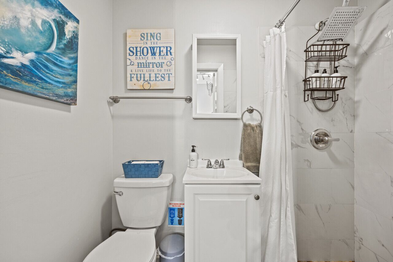 Une salle de bain équipée d’un WC, d’un lavabo et d’une douche. Il y a un panneau sur le mur et un porte-serviettes.
