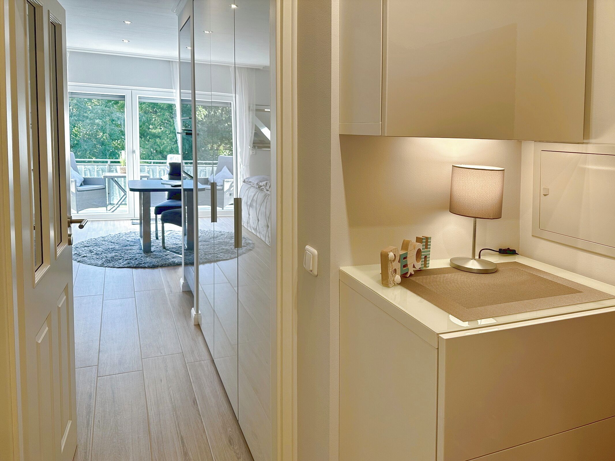 A modern kitchen with a dining area, a glass door leading to a balcony, and a small table with a lamp.