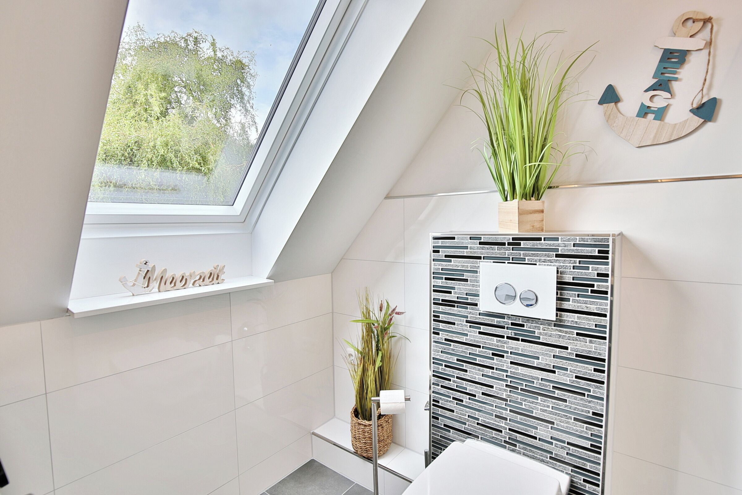 A modern bathroom with a skylight, a decorative anchor wall piece, and a potted plant.